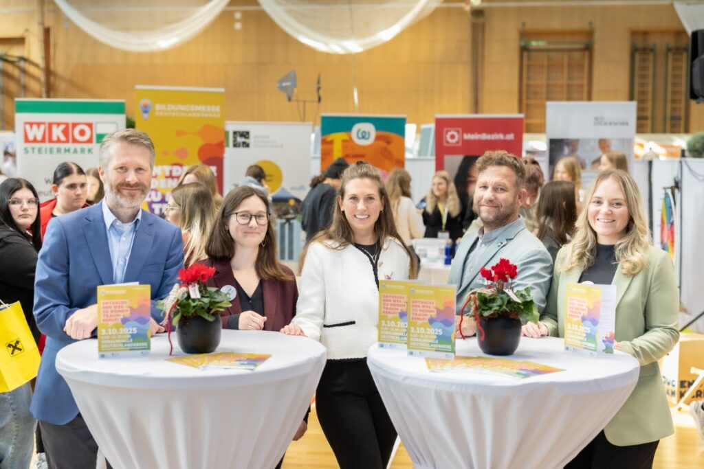 Gruppenfoto auf der Bildungsmesse in Deutschlandsberg. 2 Stehtische im Vordergrund, dahinter 5 Personen.
