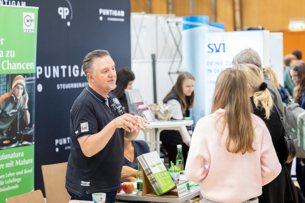 Messehalle mit Aussteller und mehreren Personen die mit ihm im Gespräch sind.